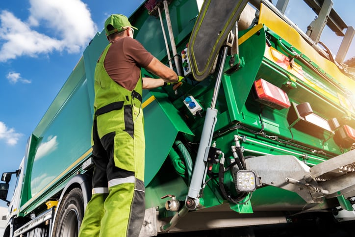 Un netturbino in azione davanti ad un camion della spazzatura