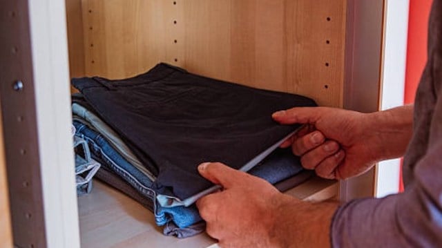 Un uomo che mette via i pantaloni nell'armadio