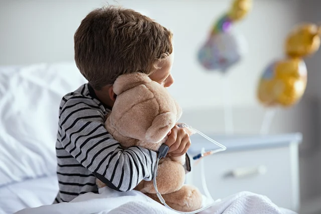 Un bambino che abbraccia un orsacchiotto dal suo letto d'ospedale