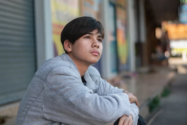 Un adolescente seduto su un marciapiede