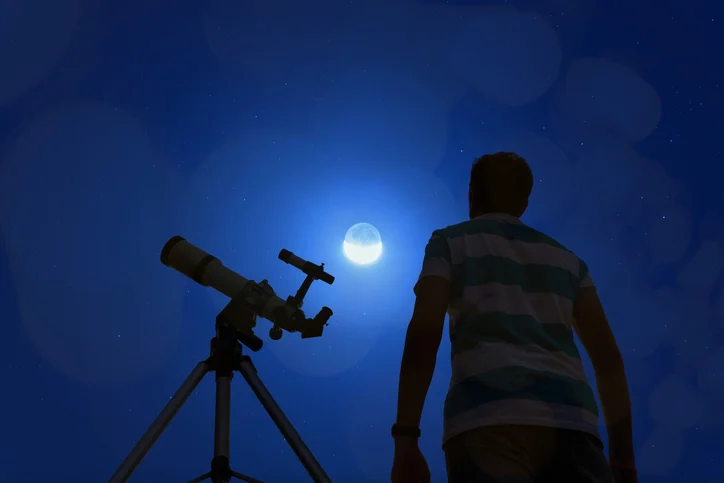 Un uomo di fronte alla Luna con un telescopio