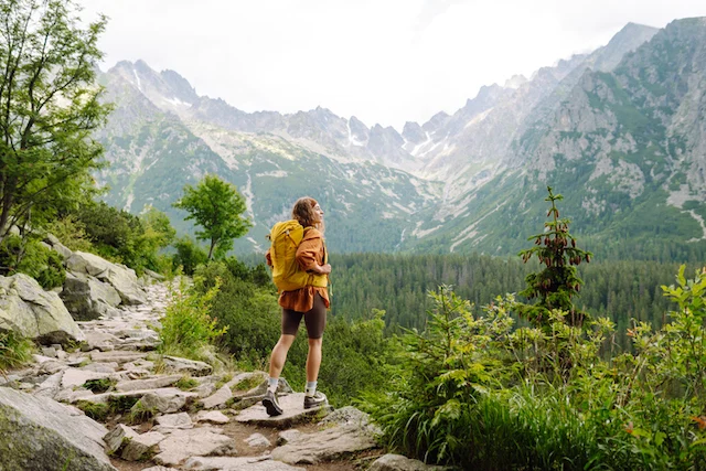 Donna felice con zaino da trekking giallo godendo del paesaggio montano