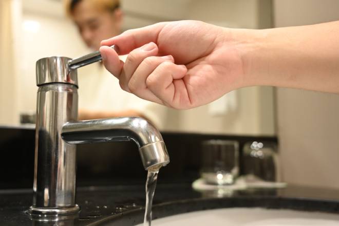 Uomo che apre un rubinetto da cui scorre un flusso d'acqua