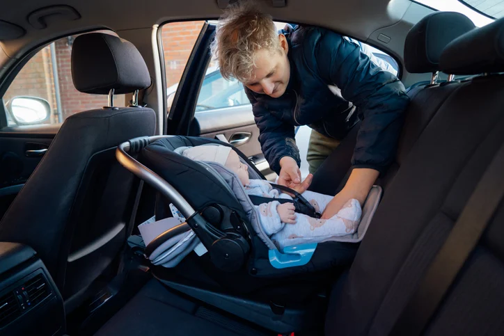 Un uomo allaccia un bambino al seggiolino di un'auto
